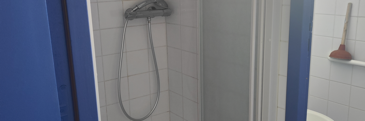 Salle de bain avec douche, pommeau, rideau, lavabo et porte-brosse.