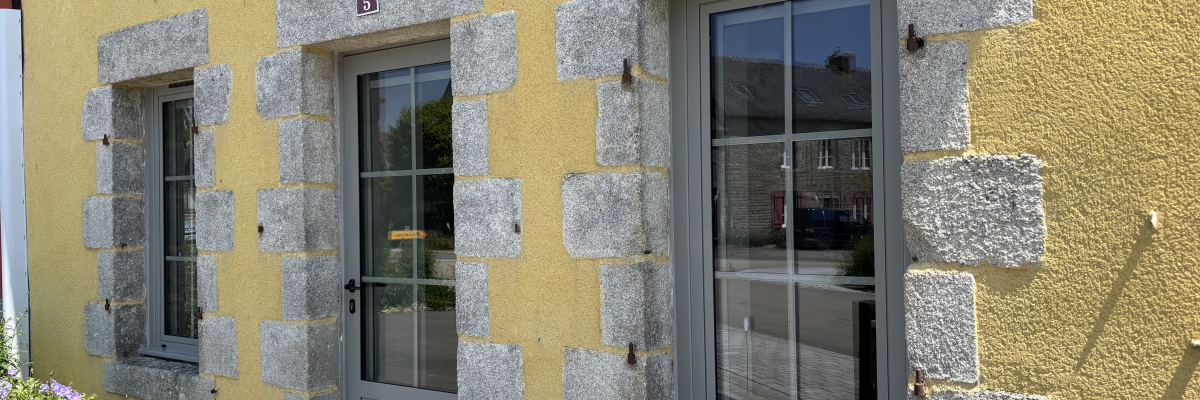 Maison jaune avec porte et fenêtres à encadrement pierreux gris.