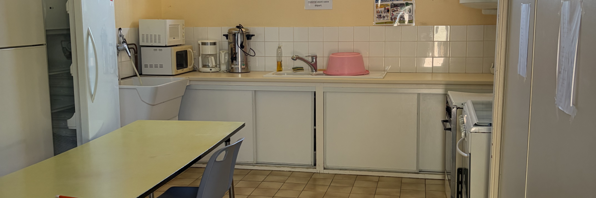 Cuisine avec réfrigérateur, table, chaises, évier, plaques de cuisson, micro-ondes et fenêtre.