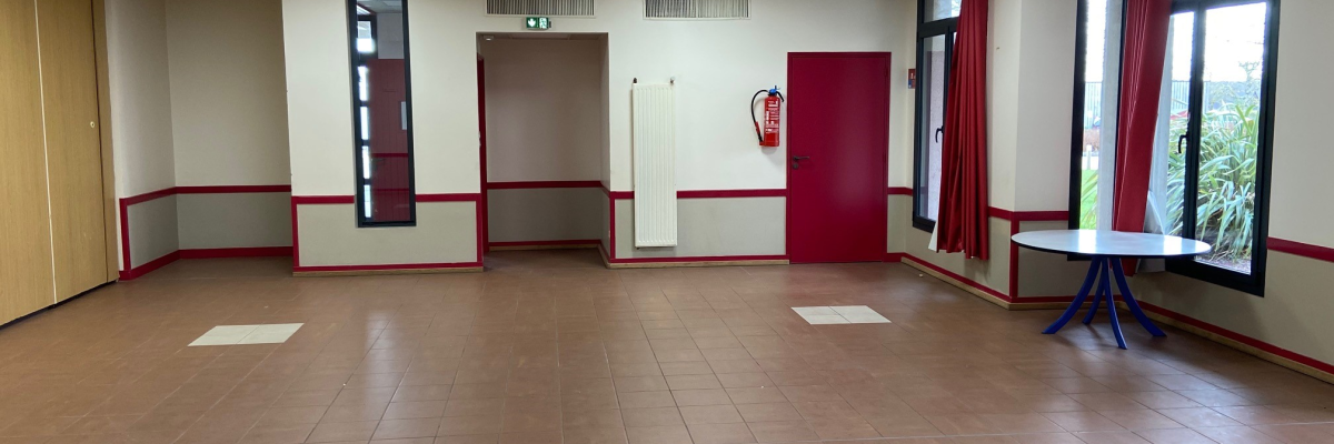 Pièce vide avec tables et chaises, armoire de rangement, climatiseur, panneaux de signalisation, et extincteur.