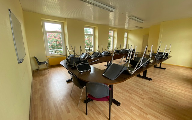 Salle avec table, chaises, tableau blanc et ordinateurs portables.