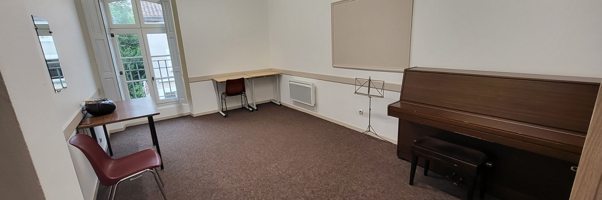 Salle avec piano, pupitre, table, chaises et porte vitrée.