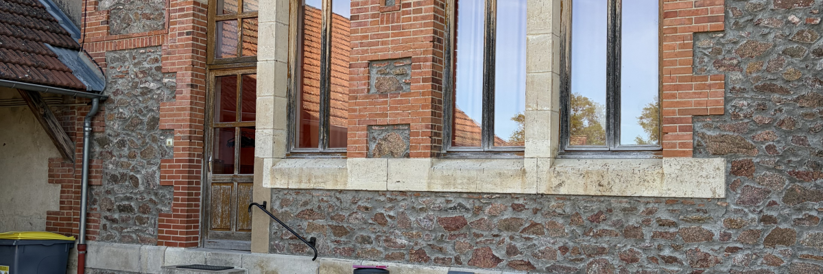 Bâtiment en brique avec grandes fenêtres, escalier extérieur et poubelle.