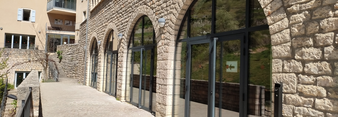 "Bâtiment en pierre avec grandes fenêtres arquées, porte en verre et balcon en pierre."