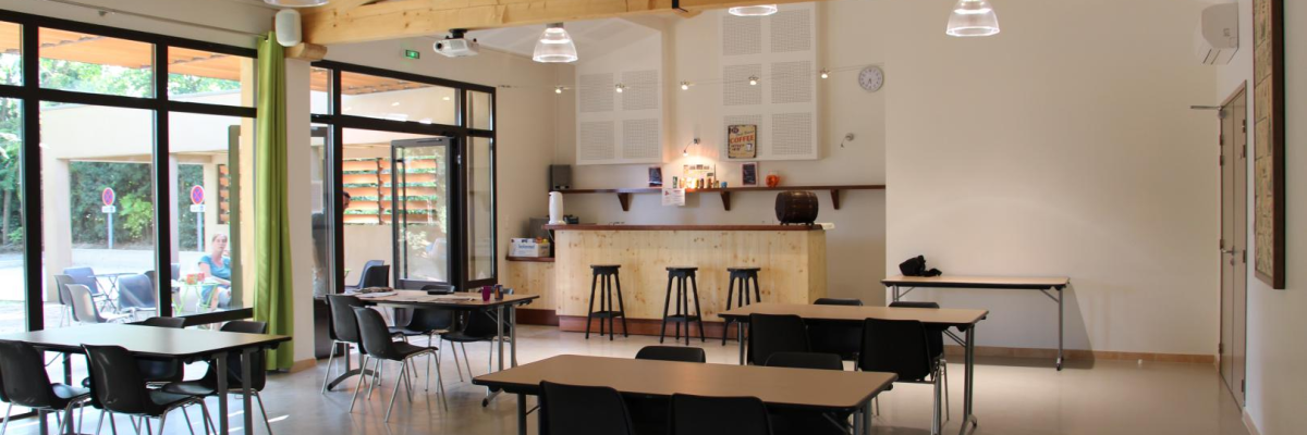 Salle avec tables, chaises, tabourets, comptoir, horloge, luminaires suspendus, porte et fenêtres.