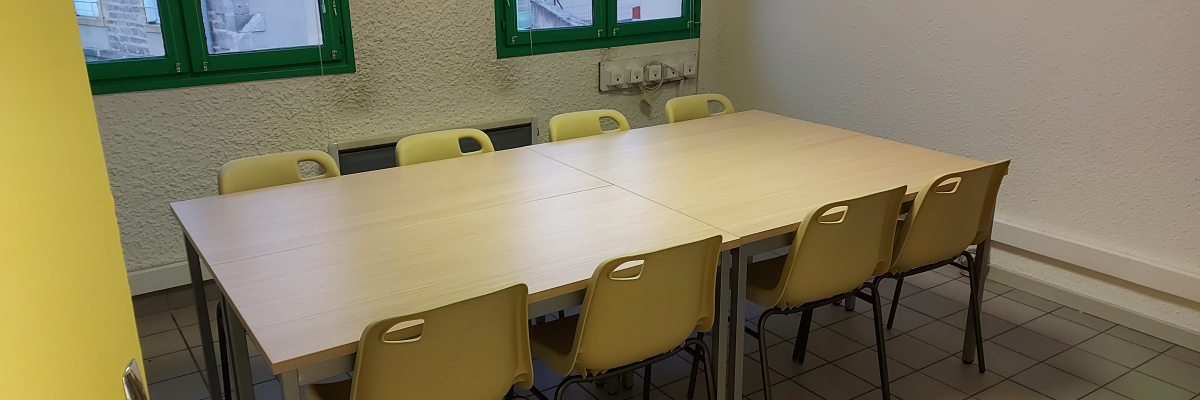 Salle avec table, chaises, fenêtres, prises murales.