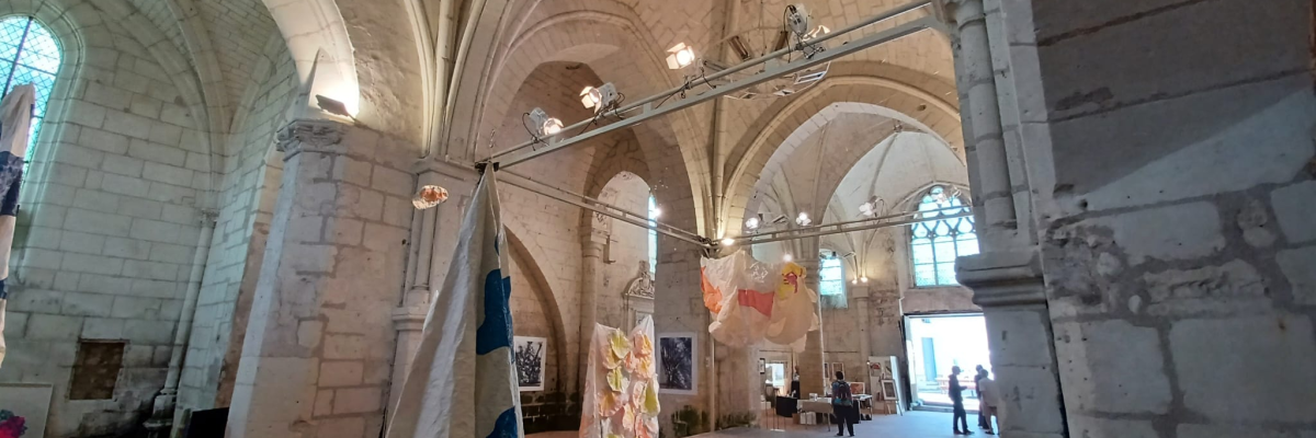 Salle voûtée avec piliers, vitraux, lustres, tentures et œuvres d'art.