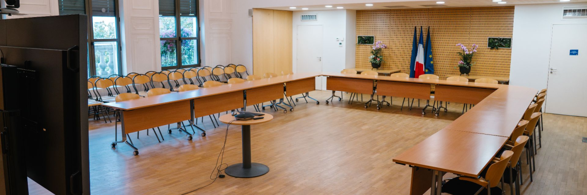 Salle de réunion avec tables, chaises, vidéo projecteur, écran et drapeau.