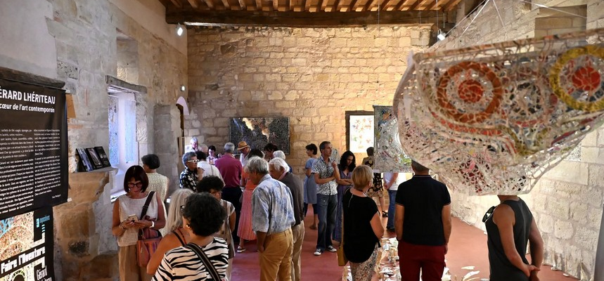 Salle d'exposition avec panneaux, sculptures, public, escalier et tissus suspendus.