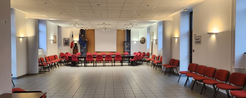 Salle de réunion avec tables, chaises, tableau, éclairage mural et plafonnier.