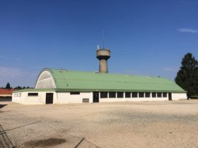 Bâtiment avec toit vert, tour de contrôle, portes et fenêtres, stationné sur une surface plane.