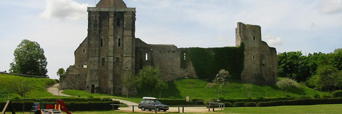 Ruines de château avec tour, voiture, aire de jeux et terrain herbeux.