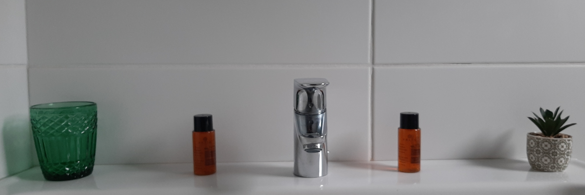 Lavabo avec robinet, deux flacons orange, vase vert et pot avec plante.