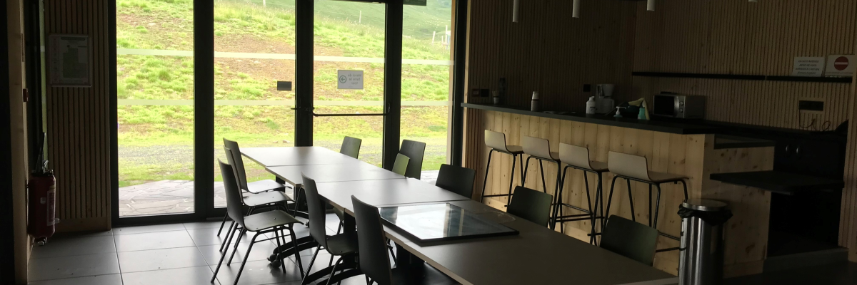 Salle avec tables, chaises, cuisine et grande porte vitrée.