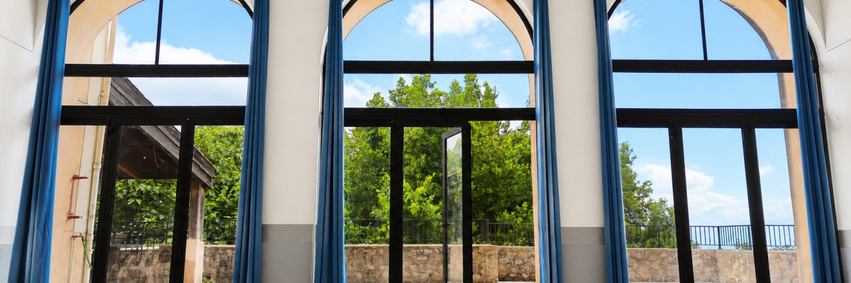 Pièce avec trois grandes portes vitrées en arc, rideaux bleus, sol carrelé, vue sur l'extérieur.
