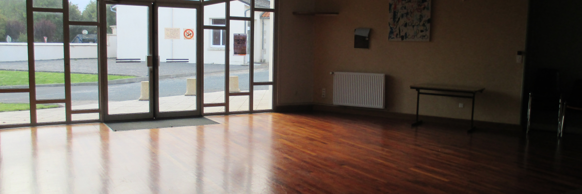 Pièce vide avec sol en bois, porte vitrée, radiateur, tableau et miroir.