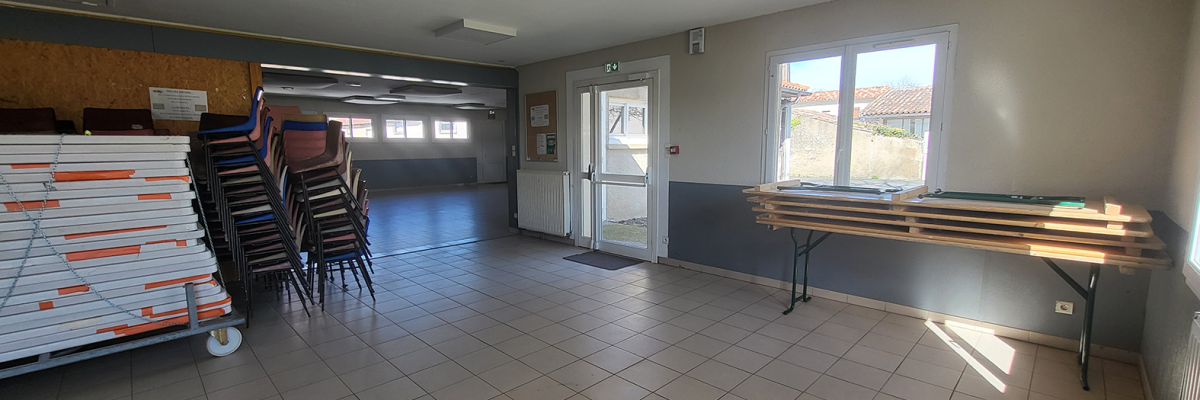 Salle avec chaises empilées, table, chariot de transport, et climatiseur mural.