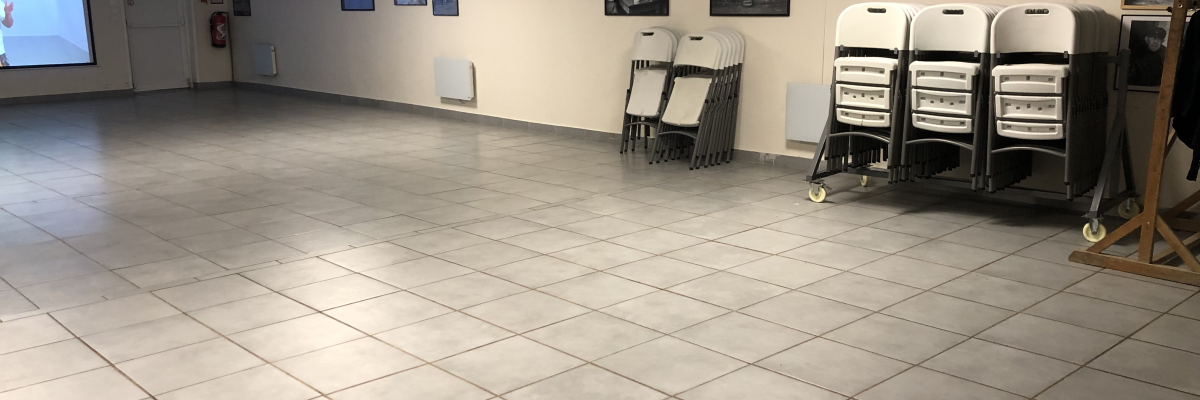 Salle avec écran, chaises empilées, rideaux, affiches et radiateurs.