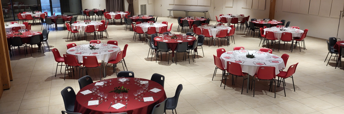 Salle avec tables rondes, chaises, nappes rouges et suspensions lumineuses.