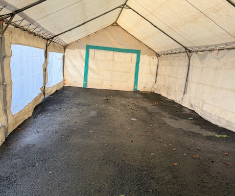 Tente vide, sol en gravier, parois blanches, porte verte.