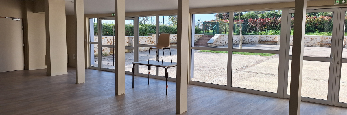 Salle vide avec portes vitrées, chaises et sol en bois.