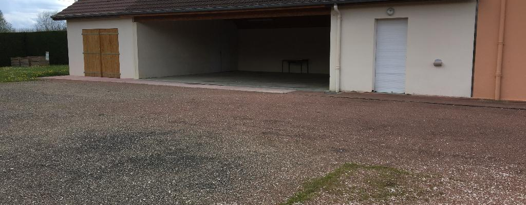 Bâtiment avec porte de garage ouverte, porte blanche et toit en tuiles.