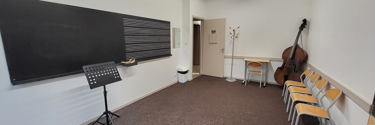 Salle de musique avec tableau, pupitre, chaises, bureau et instrument.