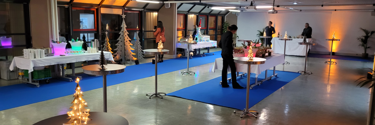 Salle avec tables, chaises, sapins, barrières et tapis bleus.
