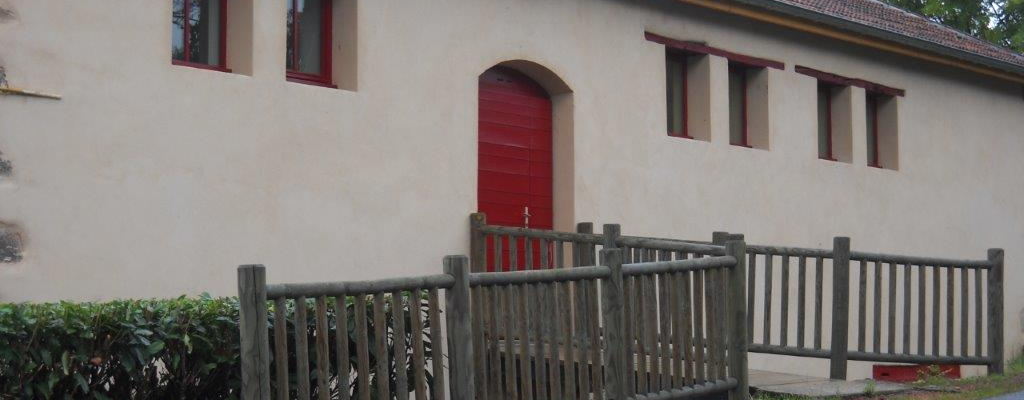 Bâtiment avec porte rouge, fenêtres et clôture en bois le long de la route.