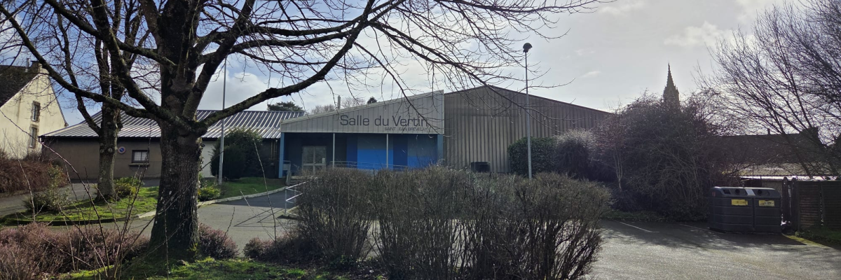 Bâtiment avec enseigne "Salle du Jeu", parking, arbre et buissons.