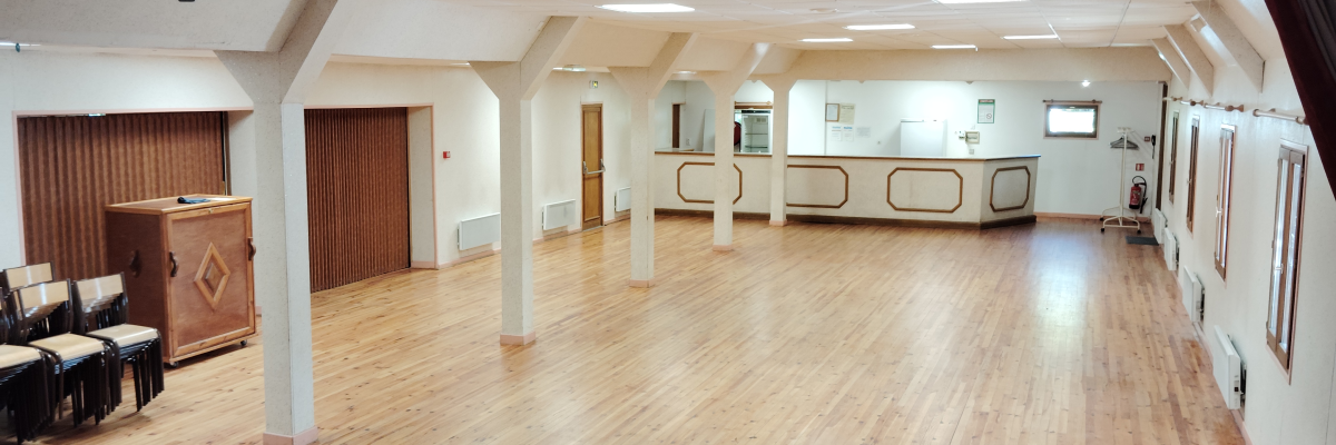 Salle avec scène en bois, projecteurs, rideau, chaises et portes.