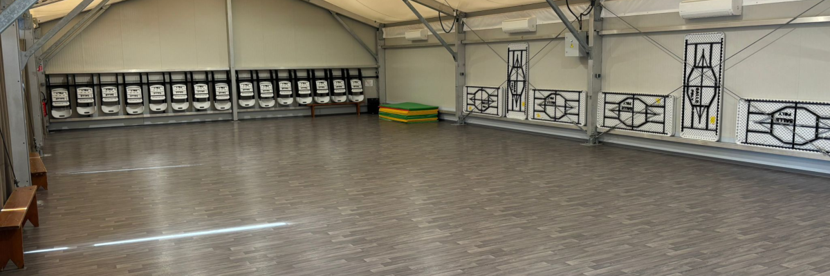 Salle spacieuse avec parquet, bancs, et fenêtres.