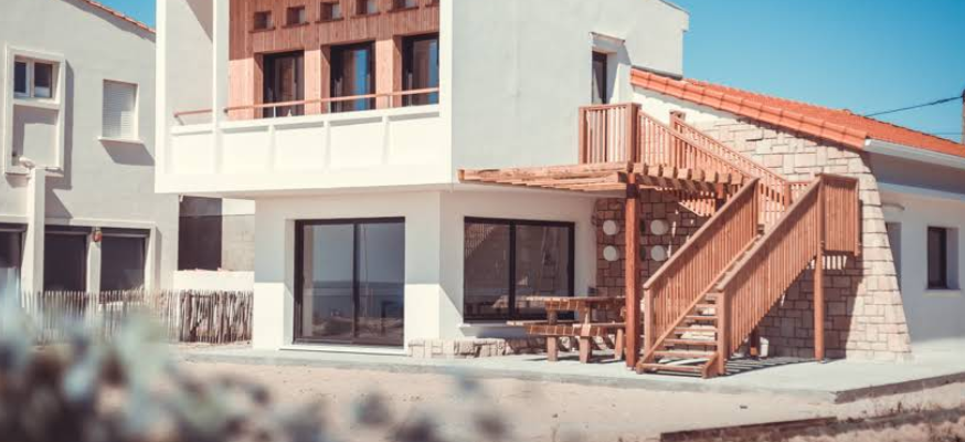 Maison moderne avec escalier extérieur en bois, grandes fenêtres et terrasse.