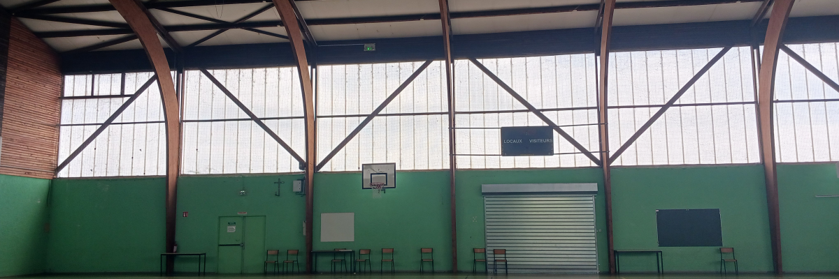 Gymnase avec paniers de basket, tableau blanc, bancs et porte de garage.
