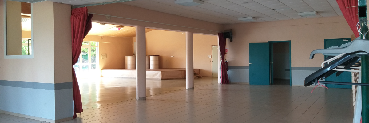 Salle vide avec portes, fenêtres, rideaux, sol carrelé, et panneaux acoustiques au plafond.