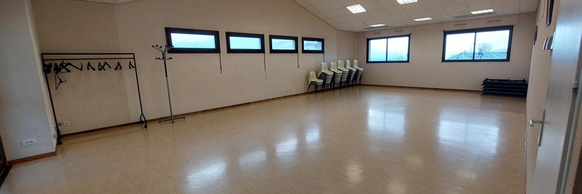 Salle avec sol en bois, bancs, fenêtres, porte, barre de danse et miroir.