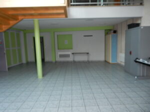 Pièce vide avec sol carrelé, piliers verts, escaliers, micro-ondes, et table avec chaises.