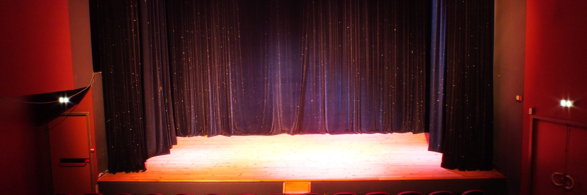 Salle de spectacle avec scène, rideaux, projecteurs, écrans latéraux et sièges.