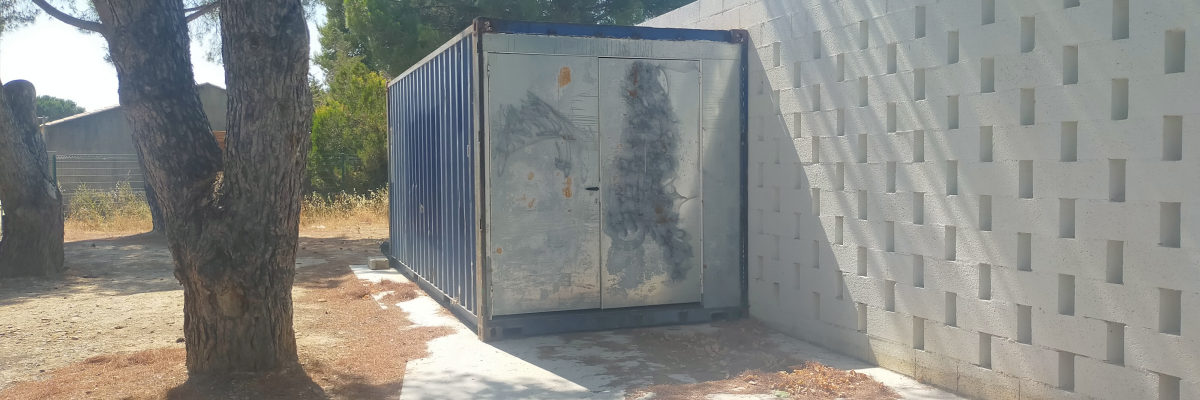 Conteneur métallique à côté d'un mur en blocs de béton. Arbre à gauche.