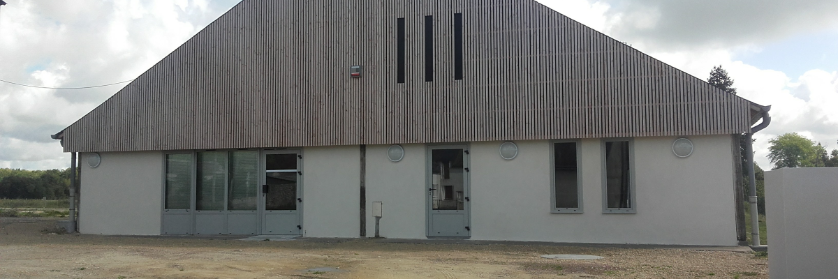 Bâtiment industriel avec toiture en tôle ondulée, fenêtres et portes en métal.