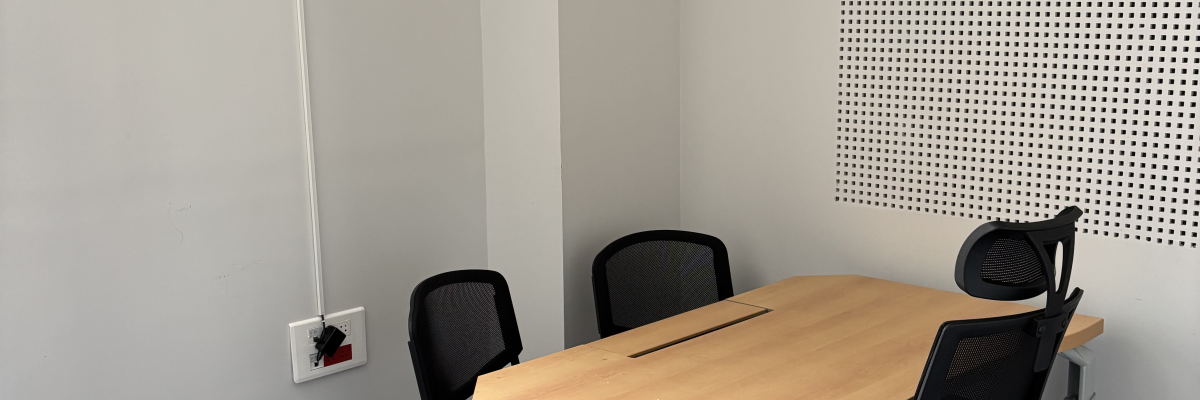 Salle avec table, chaises, ventilateur au mur et grille acoustique.