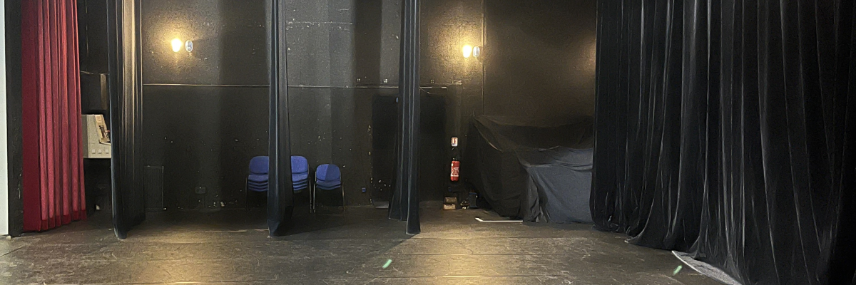 Salle vide avec rideaux, projecteurs et bancs.
