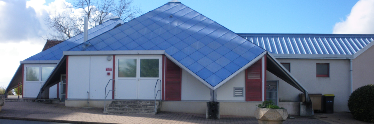 Bâtiment blanc avec toits en acier bleu, portes rouges, fenêtres, escaliers, poubelles et pot de fleur.