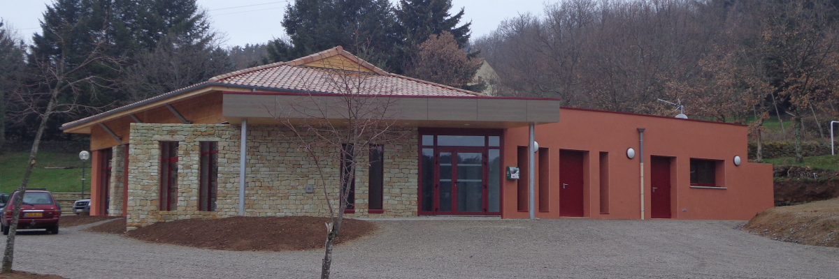 Bâtiment avec murs en brique et pierre, toit en tuiles, fenêtres et portes en verre. Voitures garées à côté.