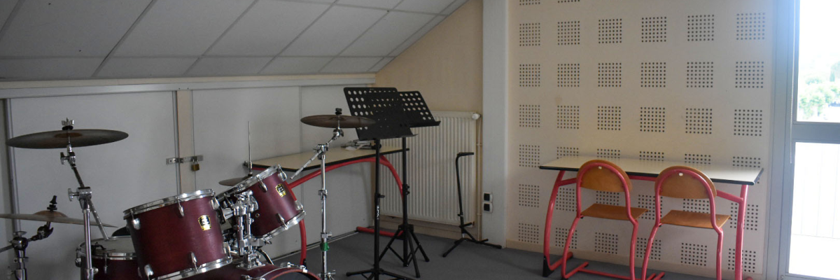 Pièce avec batterie, pupitre, ampli, chaises et tableau d'acoustique.