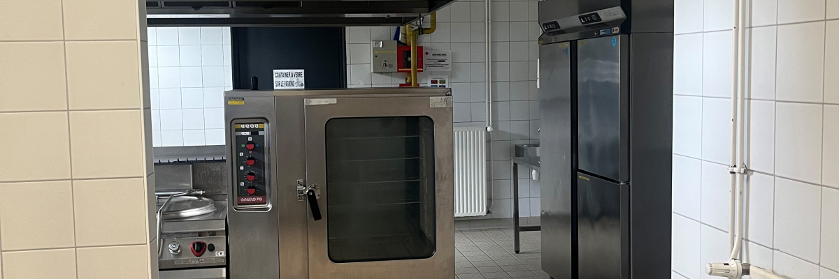 Cuisine professionnelle avec four, hotte, réfrigérateur et plans de travail.