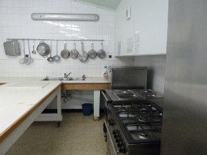 Cuisine avec plans de travail, cuisinière, étagères, ustensiles suspendus et évier.