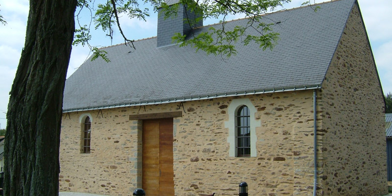 Bâtiment en pierre avec porte en bois, banc et poubelle devant.