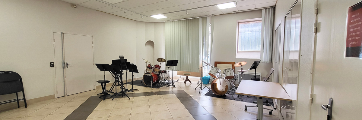 Salle de musique avec batterie, piano électrique, chaises, pupitres.