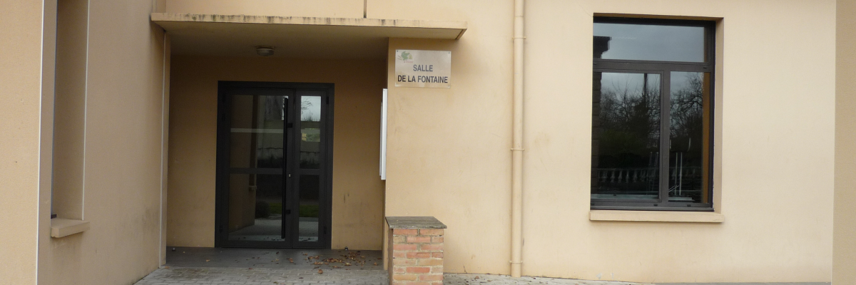 Entrée d'un bâtiment avec porte, fenêtres et panneau indiquant la salle de la fontaine.